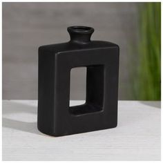 a black square vase sitting on top of a white table next to a green plant