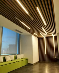 a green couch sitting in front of a window next to a wooden ceiling with lights on it