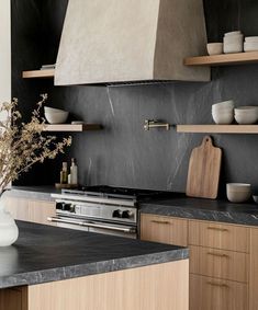 a kitchen with black counter tops and wooden cabinets, an oven hood over the stove