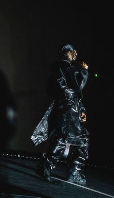 a man in black jacket and pants standing on top of a roof holding a cell phone to his ear