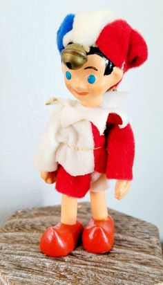 a small toy doll wearing a red and white outfit with blue eyes on top of a wooden table