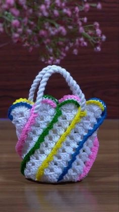 a crocheted basket sitting on top of a wooden table next to a pink flower