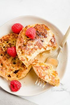 pancakes with raspberries and butter on a white plate next to a knife and fork