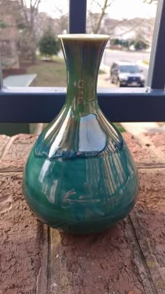 a green vase sitting on top of a wooden table next to a window sill