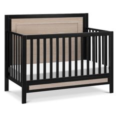 a black crib with a white sheet on the bottom and beige bedding underneath it