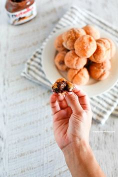 a person holding a piece of food in front of a plate of doughnuts