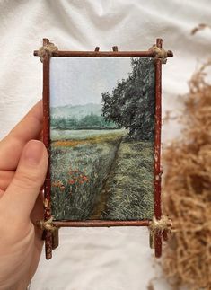 a person holding up a small piece of art with grass and trees in the background