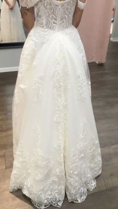 a woman in a wedding dress looking at herself in the mirror with her hand on her hip