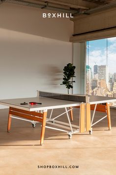 A white folding outdoor ping pong table set on a modern indoor space with large glass window with a view of a city skyline Outdoor Ping Pong Table, Ping Pong Table