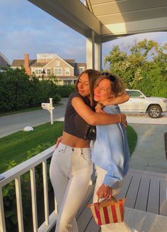 two women standing on a porch hugging each other and holding shopping bags in their hands