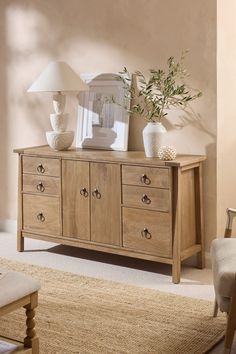 a wooden dresser with two vases and a lamp on top of it in a living room