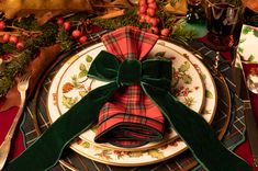 a christmas place setting with green velvet bows and plaid napkins on the plate, along with other holiday decorations