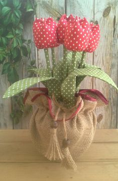 a vase filled with red flowers sitting on top of a wooden table next to a green plant