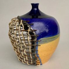 a blue and yellow vase with some strings in it's bottom half, on a white surface