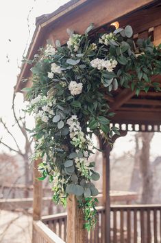 a wooden gazebo decorated with greenery and white flowers