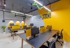 an office with yellow chairs and black desks in front of a big sign that says think big