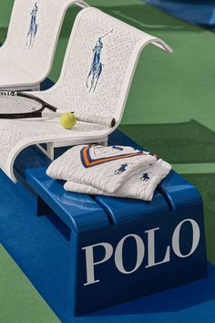 two white chairs sitting on top of a tennis court next to a ball and racket