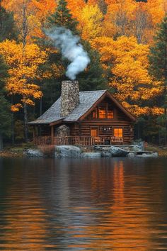 a log cabin sits on the edge of a lake surrounded by trees with yellow leaves