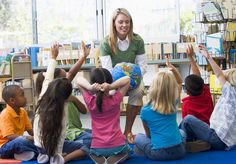 a woman is sitting in front of children and raising their hands to the sky while they sit on the floor