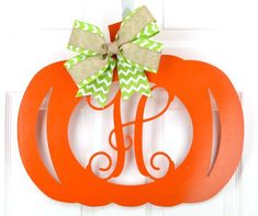 an orange pumpkin shaped door hanger with a monogrammed bow on the front