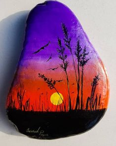 a painted rock sitting on top of a white table next to a tree and sunset