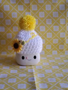 a small white cup with a yellow flower on it and a knitted hat in the shape of a pom pom