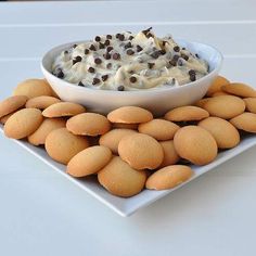 a white plate topped with lots of cookies next to a bowl filled with whipped cream