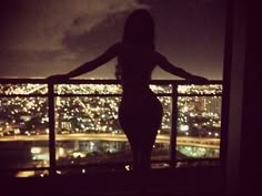 a woman standing in front of a window with her arms spread out and looking at the city lights