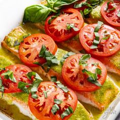 fish covered in pesto and tomatoes on a white platter with fresh basil garnish