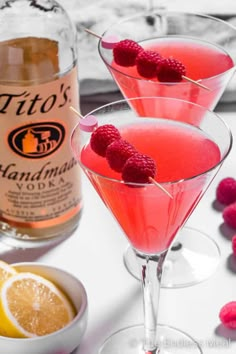 two martinis with raspberries sit in front of a bottle of booze