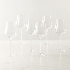 six wine glasses lined up on a marble countertop with white walls in the background