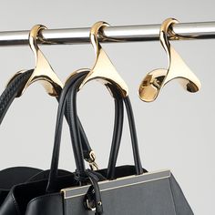 a black purse hanging from a metal bar with gold handles and two matching handbags