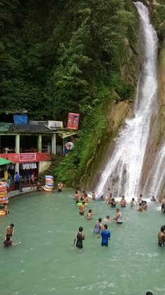 many people are in the water near a waterfall