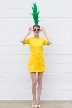 a woman in a yellow dress with a green pineapple on her head and sunglasses