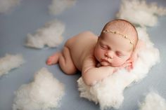 a newborn baby is sleeping on some fluffy white clouds and wearing a gold headband