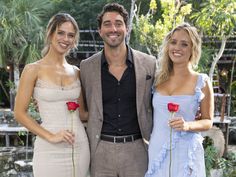 two women and a man standing next to each other in front of a fountain holding roses