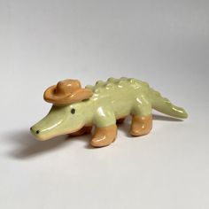 a ceramic toy alligator with a hat on its head and legs, sitting on a white surface