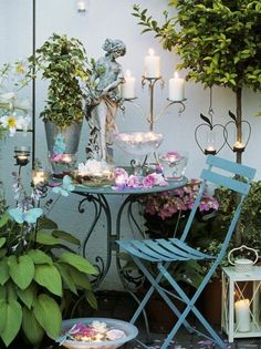 a small table with flowers and candles on it in front of a white wall surrounded by potted plants