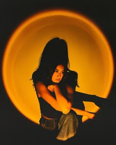 a woman sitting in front of a yellow circle with her hands on her hips and looking at the camera