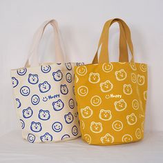 three bags with smiley faces on them are lined up against a white wall, one is yellow and the other is blue