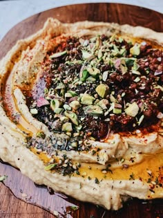 an assortment of food on top of a wooden platter, including hummus and olives