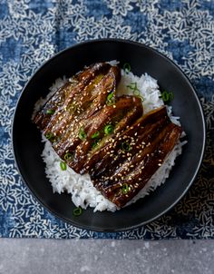 a black plate topped with meat and rice on top of a blue table cloth next to a fork