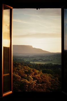 an open window shows the view of mountains and trees from inside a room with large windows