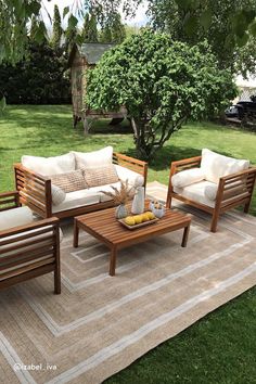 an outdoor living area with wooden furniture and rugs on the grass, surrounded by trees