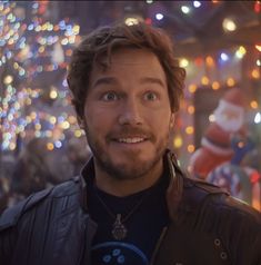 a man in a leather jacket is smiling at the camera with christmas lights behind him