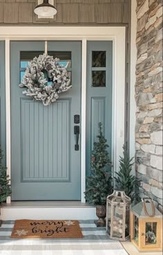 a blue front door with two wreaths and christmas trees on the side walk next to it