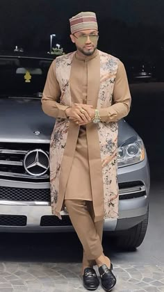 a man standing in front of a car wearing a turban and holding his hands together