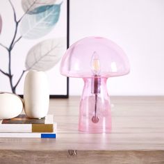 a pink lamp sitting on top of a wooden table next to books and a vase