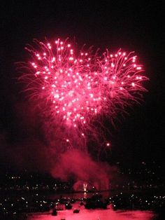 fireworks are lit up in the night sky above water and boats on the river below