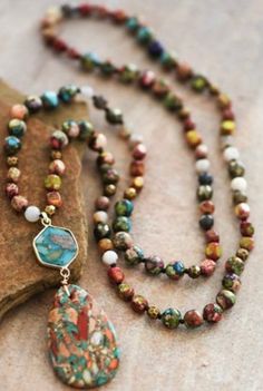 a long beaded necklace with a stone heart pendant on it's end, sitting next to a rock